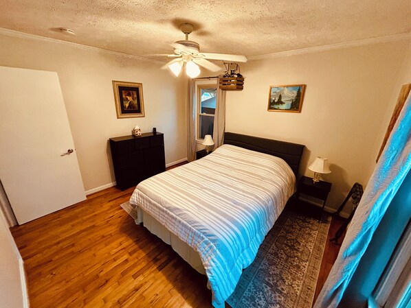 A bedroom with a bed, dresser, ceiling fan, and artwork on the walls.