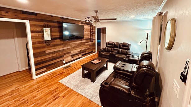 A modern living room with a wooden wall, a flat-screen TV, leather sofas, and a ceiling fan. - Little House in Jasper (Jasper)