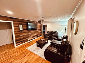 A modern living room with a wooden wall, a flat-screen TV, leather sofas, and a ceiling fan.