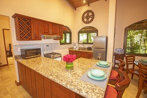 Une cuisine dotée de plans de travail en granit, d’armoires en bois, d’un îlot central, d’une cuisinière, d’un four à micro-ondes et d’un réfrigérateur.
