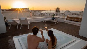 Ein Paar in einer Whirlwanne auf einer Dachterrasse mit Sonnenuntergangblick.