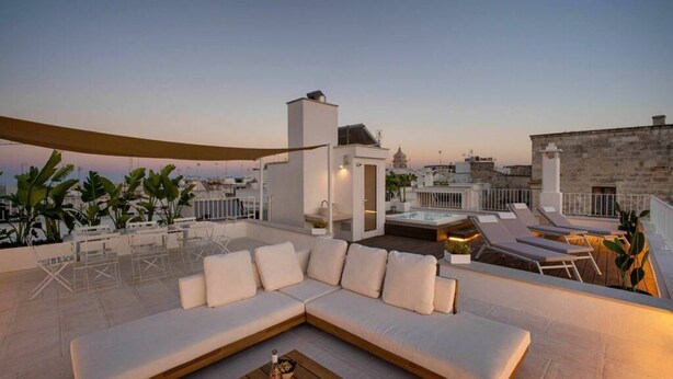 Eine Dachterrasse mit einem weißen Sofa, Lounge-Stühlen und einem Holztisch.