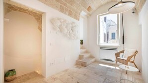 Ein Zimmer mit Steindecke, einem Korbstuhl, einem kleinen Tisch und einer Treppe zu einem Fenster.