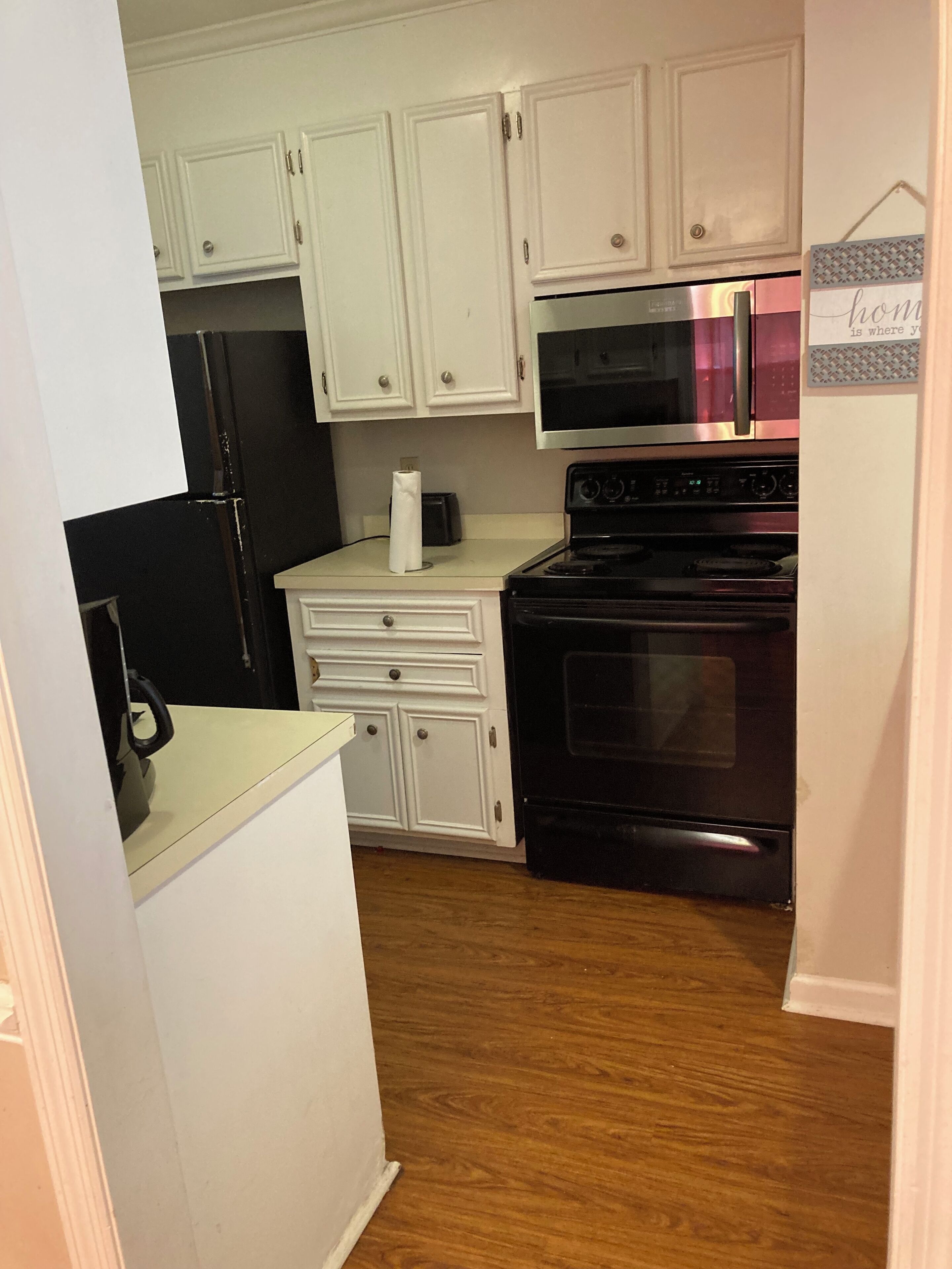 A compact kitchen with white cabinets, a black refrigerator, a microwave, and an oven.