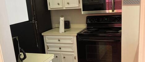 A compact kitchen with white cabinets, a black refrigerator, a microwave, and an oven.