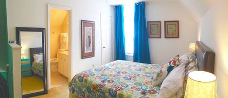 A bedroom with a bed, a bedside lamp, a mirror, and a door leading to a bathroom.