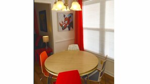 Ein Essbereich mit einem runden Tisch, roten Stühlen, einer Chandelier und einem Fenster mit Jalousien.