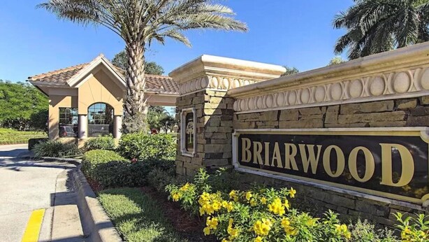 Señal de Briarwood con un muro de piedra y flores amarillas al frente.