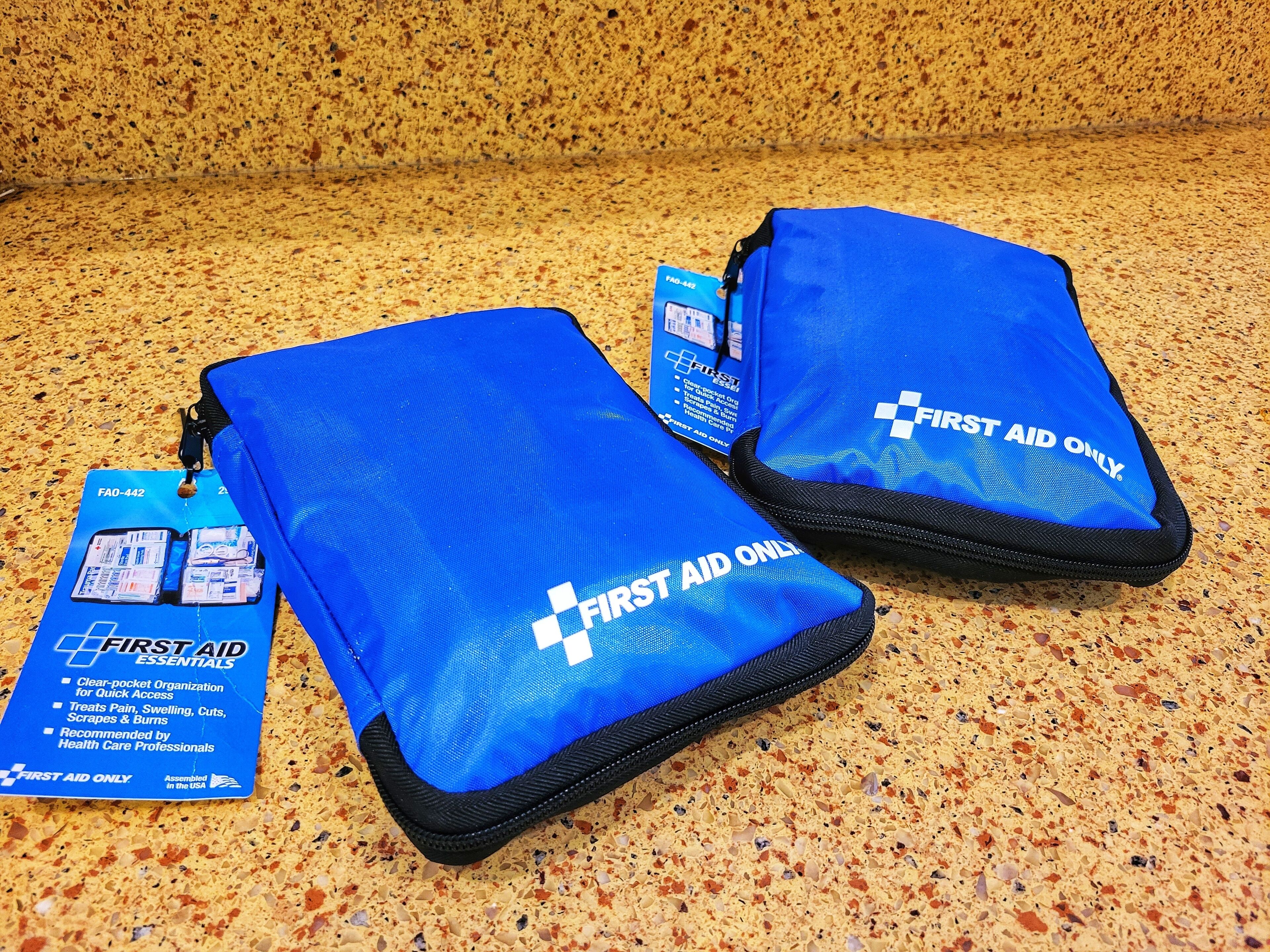 Two blue first aid kits with tags on a speckled countertop.
