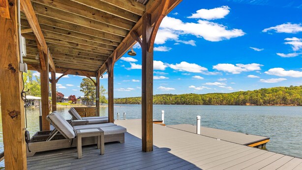 A wooden deck with lounge chairs and a covered area overlooking a lake.