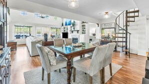 A spacious dining area with a glass-top table, wooden chairs, and a modern staircase.