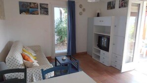 Un salon comprenant un canapé, un téléviseur posé sur un meuble, une table à manger et une porte-fenêtre coulissante donnant sur un espace extérieur.