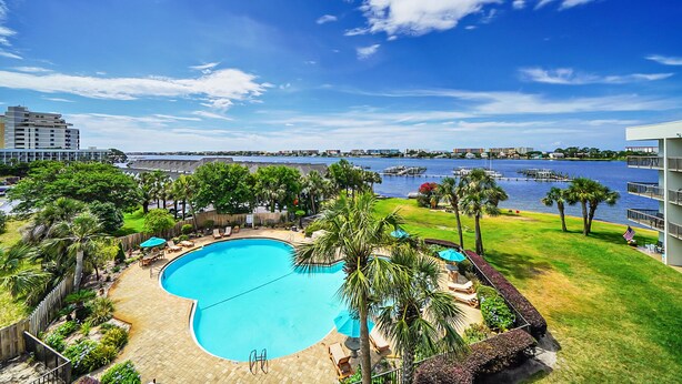 A swimming pool surrounded by palm trees and a view of a body of water. - Waterfront Condo w/Pool Access (Fort Walton Beach)