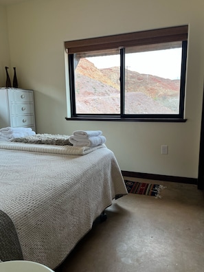Une chambre à coucher comprenant un lit, une commode, une fenêtre donnant sur un paysage rocheux et un tapis.