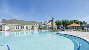 Una piscina con sillas de descanso y un edificio con varias ventanas y una chimenea.