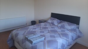 Un lit bien fait, recouvert d’une couvre-lit à motifs, une table de chevet avec une lampe et un radiateur fixé au mur.