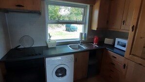 Une cuisine compacte avec des meubles en bois, un lave-linge, un four à micro-ondes et une fenêtre donnant sur un espace verdoyant.