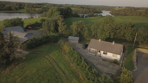 Vue aérienne d’une zone rurale avec une maison, une petite grange et une étendue d’eau.