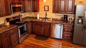 Una cocina con gabinetes de madera, encimeras de granito, electrodomésticos de acero inoxidable y piso de madera.