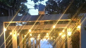 Un sendero bajo una pérgola con luces de cadena, que lleva a una masa de agua.