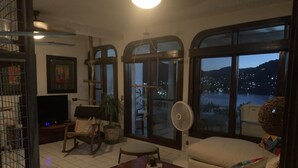 En stue med fjernsyn, ventilator, sofa og udsigt til en sø om natten.