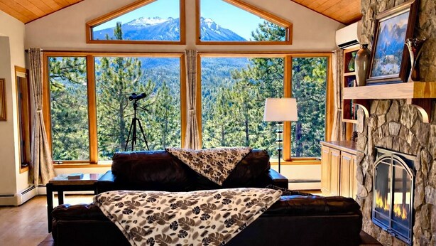 Un salon chaleureux doté d’une grande fenêtre donnant sur les montagnes, d’une cheminée et d’un mur en pierre.