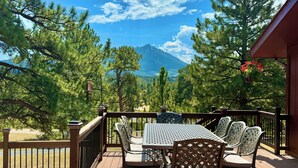 Une terrasse en bois avec une table et des chaises, offrant une vue sur un paysage montagneux.