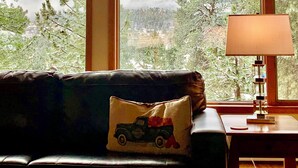 Une pièce dotée d’une grande fenêtre donnant sur les montagnes, d’un canapé en cuir avec un coussin et d’une lampe sur une table d’appoint.