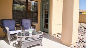 An outdoor patio with wicker furniture, a glass table, and a door leading to the interior. - 2-Bedroom Condo in the Foothills, La Encantada, Galleries and Restaurants! (Tucson)