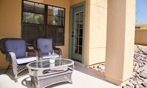 An outdoor patio with wicker furniture, a glass table, and a door leading to the interior.