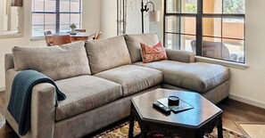 A beige sectional sofa with a throw blanket, a small wooden coffee table, and a window with blinds.