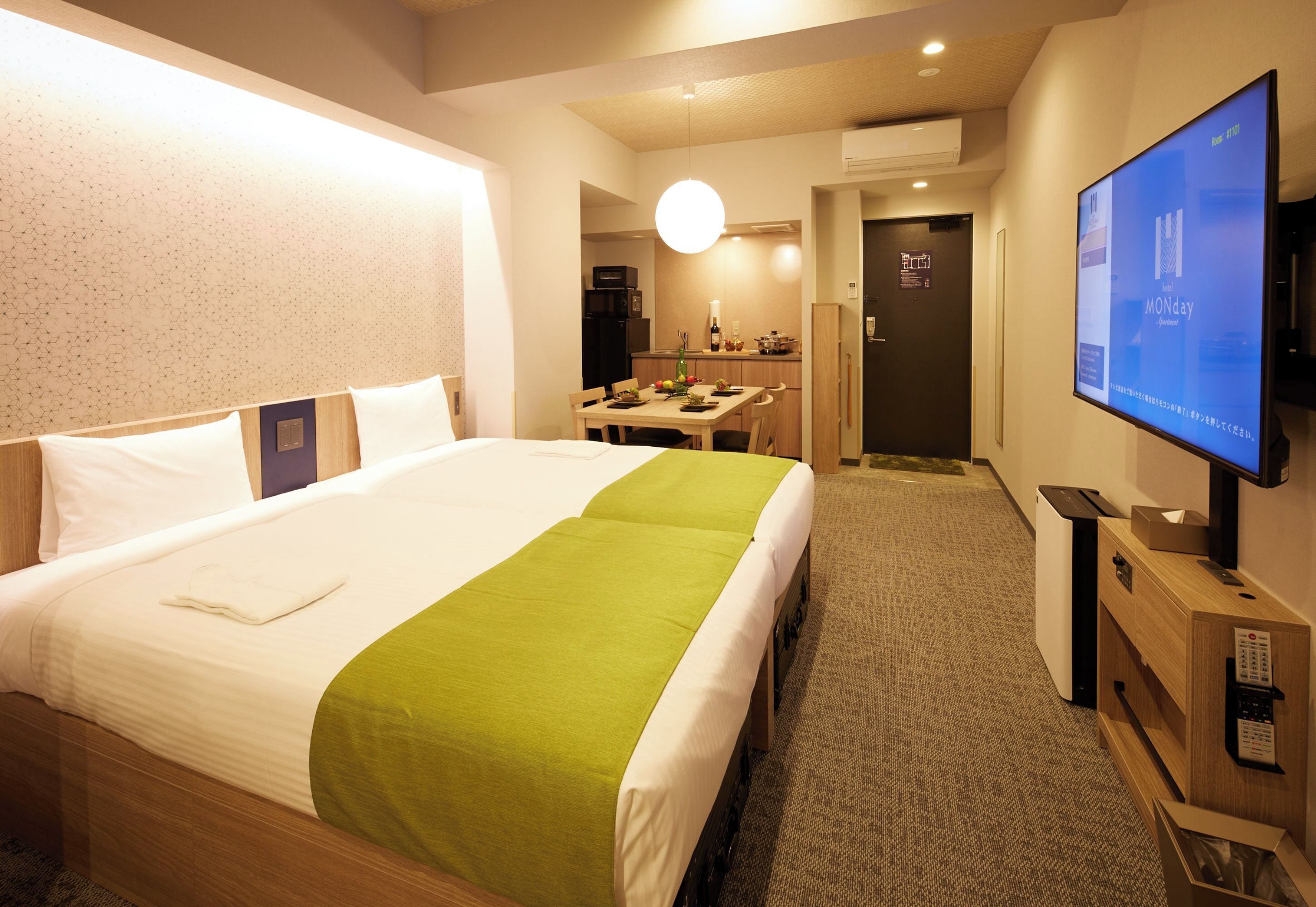 A hotel room with a bed, a desk, a television, and a kitchenette.