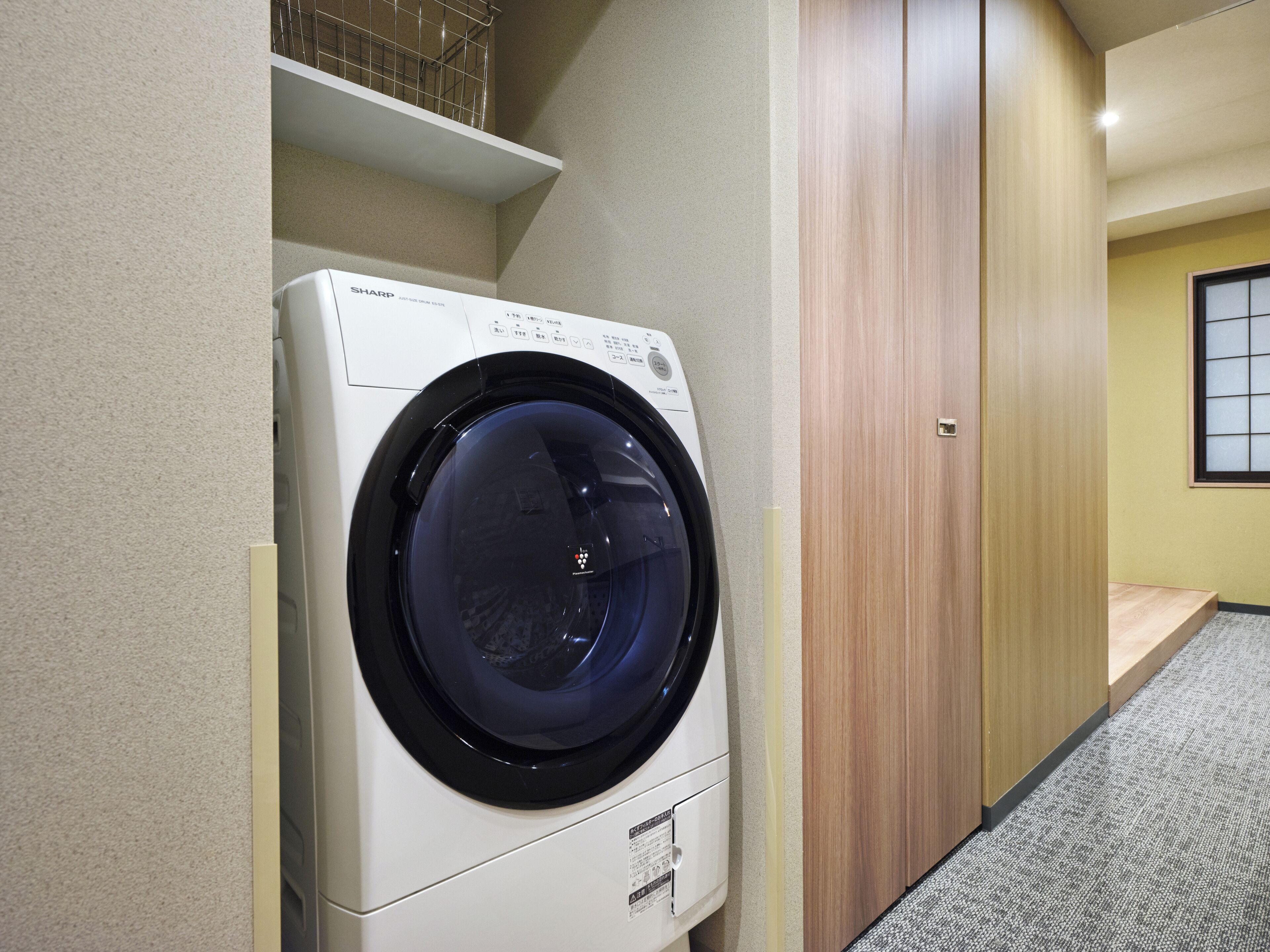 A compact, modern laundry room with a front-loading washing machine, wooden cabinets, and a small window.