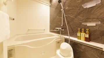 Ein Badezimmer mit Badewanne, Dusche und Marmorwand. Auf einem Regal befinden sich Toilettenartikel.