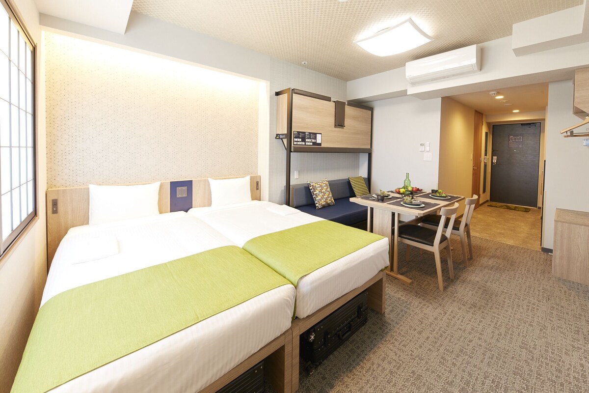 A hotel room with a bed, a desk, a chair, and a small kitchenette.