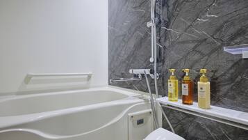 A modern bathroom with a bathtub, a shower, and a marble wall. There are three bottles of toiletries on a shelf.
