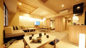 A modern living room with a sofa, a dining table with tea set, and a TV in the background. - MONday Apart Premium Ueno (Tokyo)