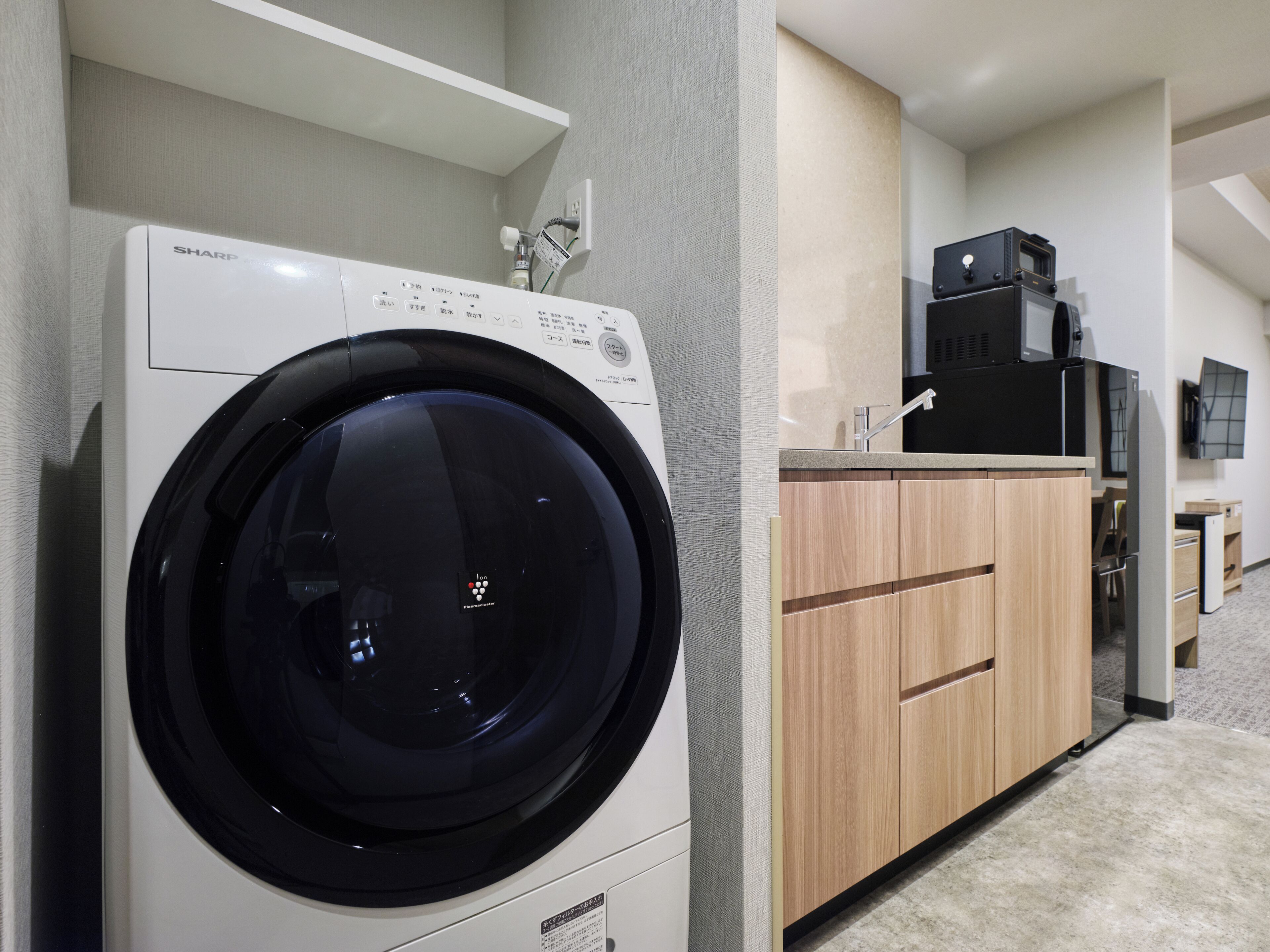 Un espace buanderie compact comprenant un lave-linge à chargement frontal, des placards en bois et un four à micro-ondes.