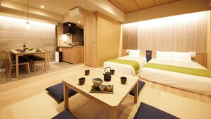 A hotel room with a dining area, a bed with a green bedspread, a bedside table with a teapot and cups, and a small kitchenette. - MONday Apart Premium Ueno (Tokyo)
