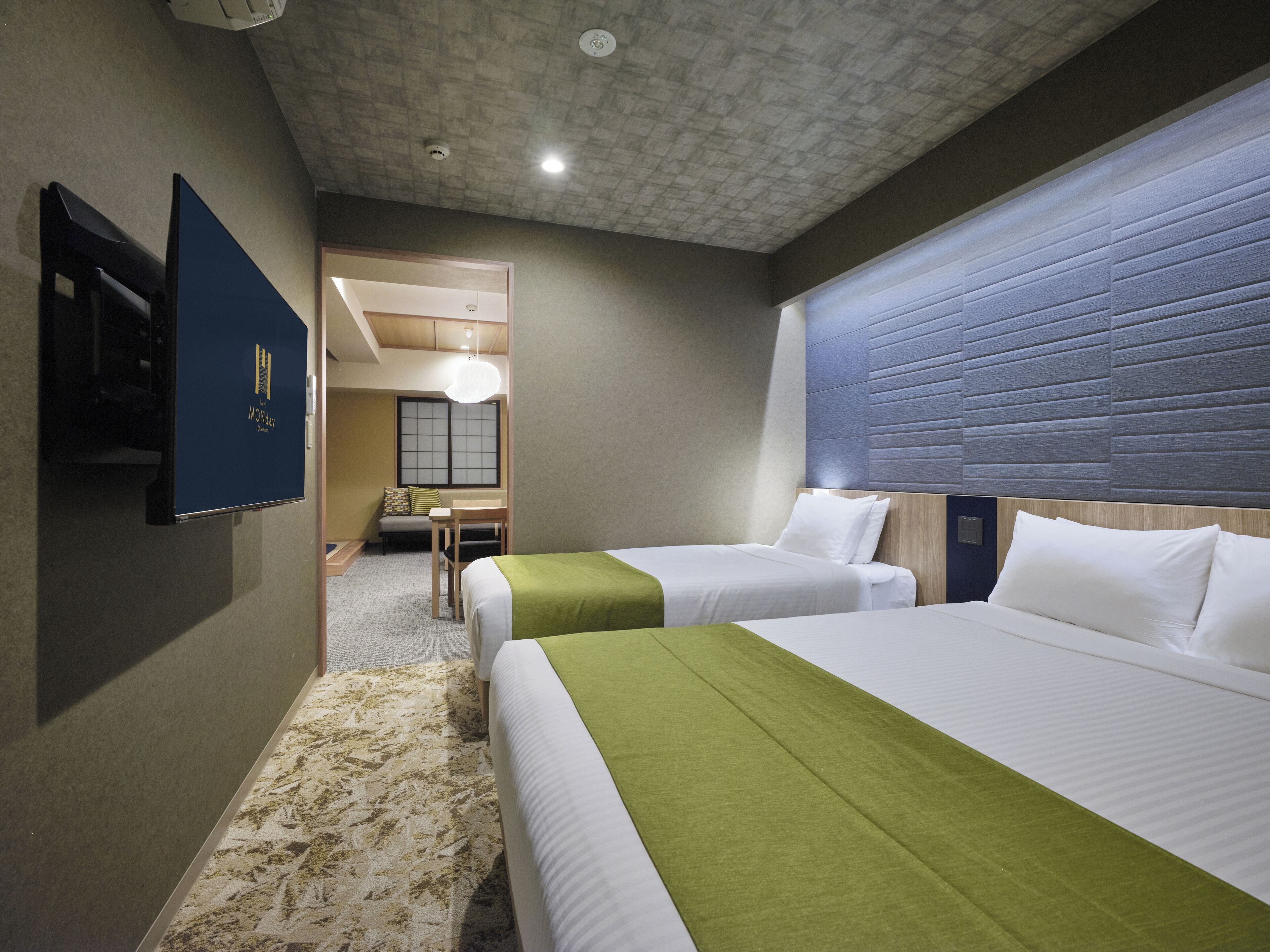 Een hotelkamer met twee bedden, een bureau en uitzicht op een traditionele Japanse kamer.