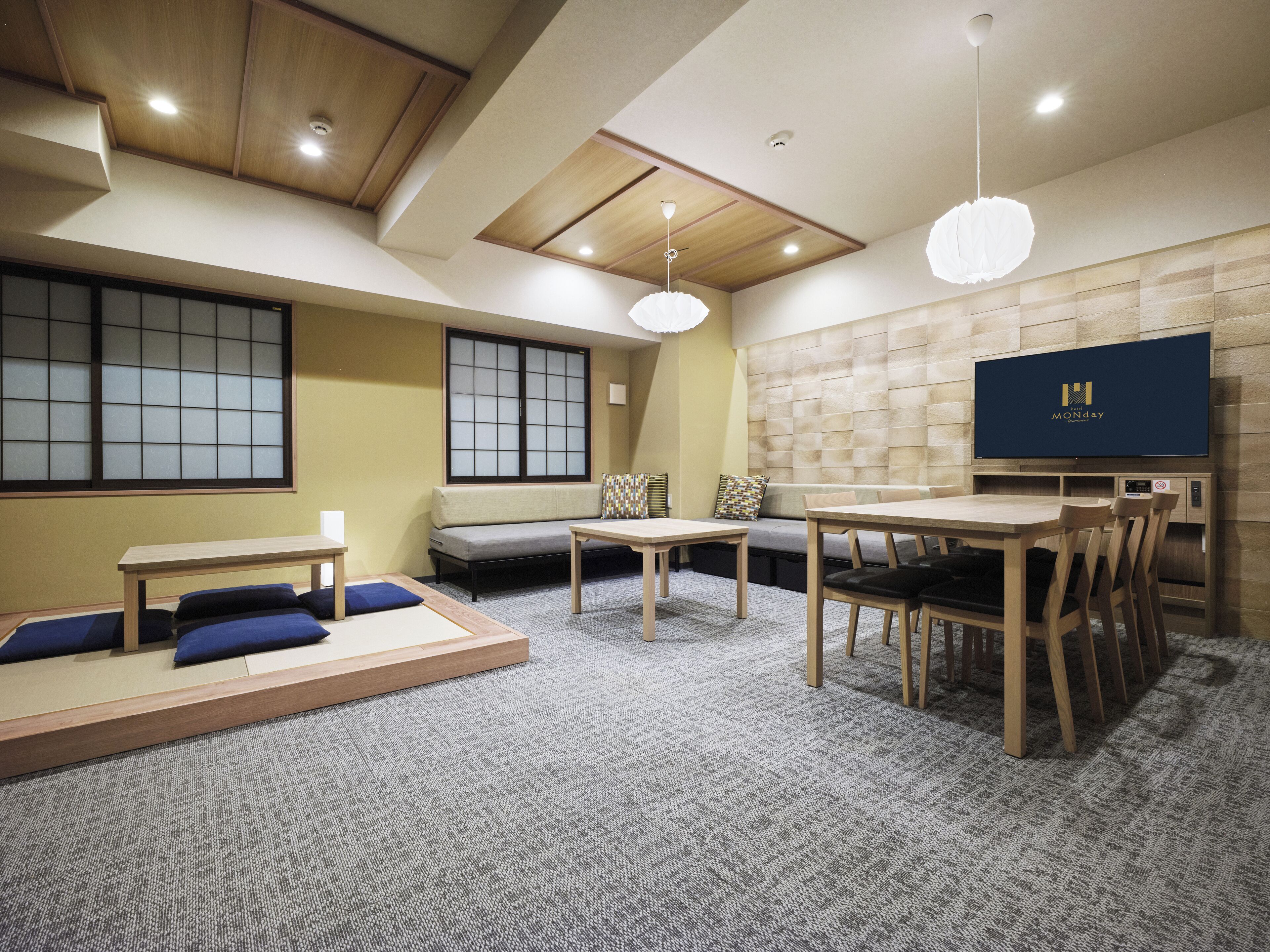 Une chambre d’hôtel moderne au décor d’inspiration japonaise traditionnelle, comprenant des tatamis, une table basse, un canapé et un téléviseur fixé au mur.