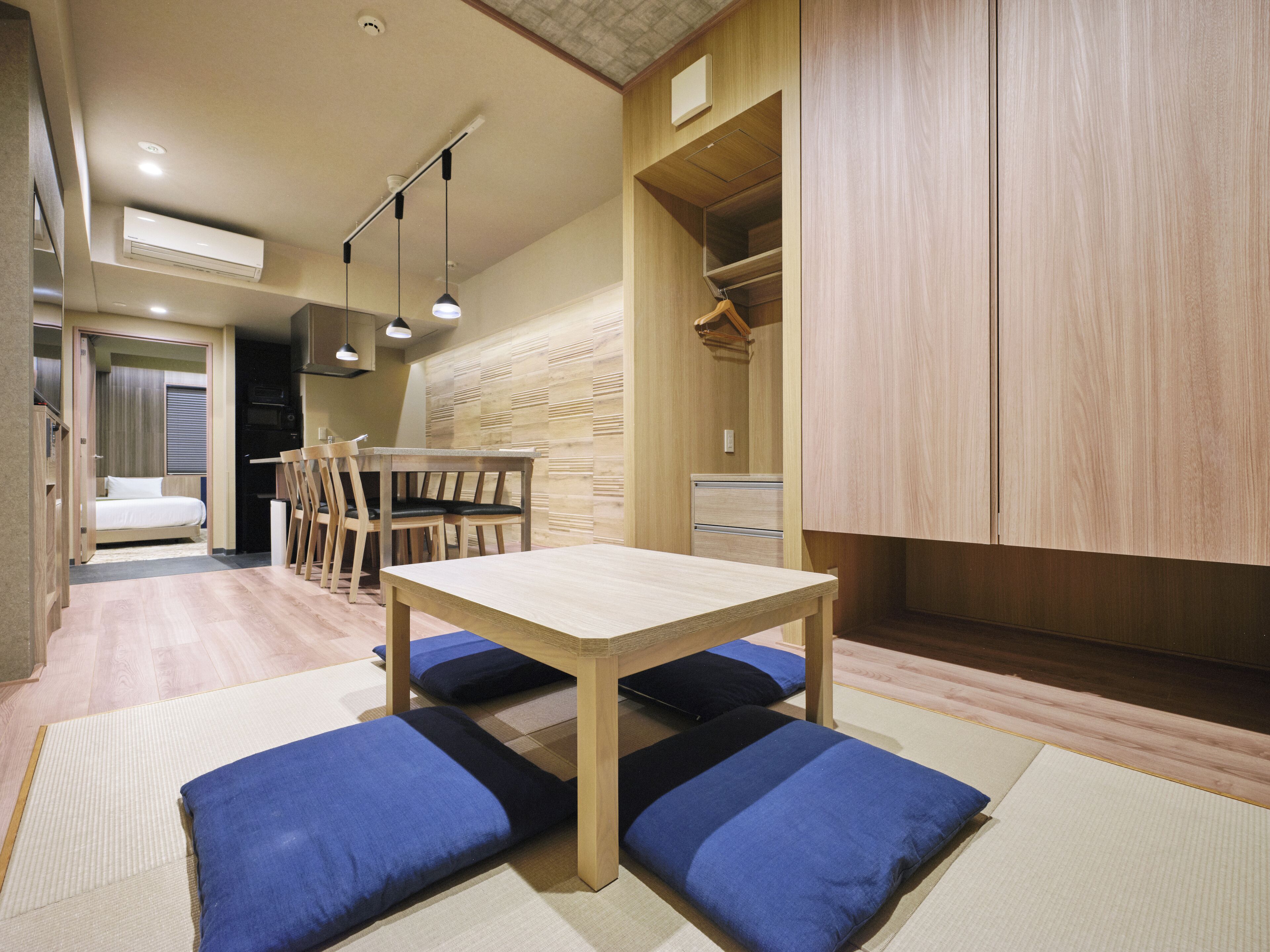 A compact room with a wooden dining table, chairs, and a sofa with blue cushions.