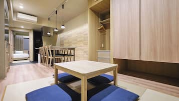 A compact room with a wooden dining table, chairs, and a sofa with blue cushions.