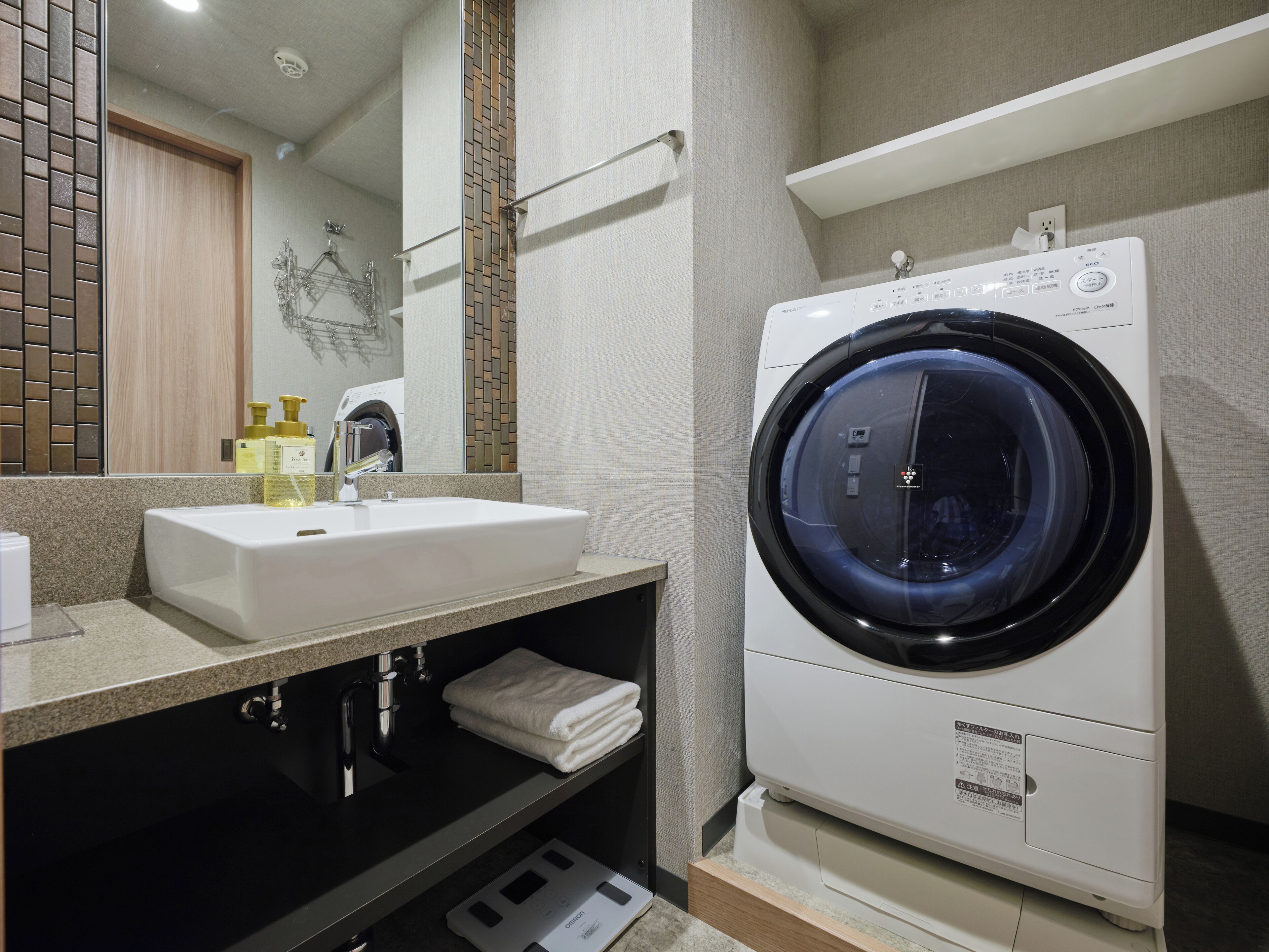 A modern bathroom with a sink, mirror, and a front-loading washing machine.