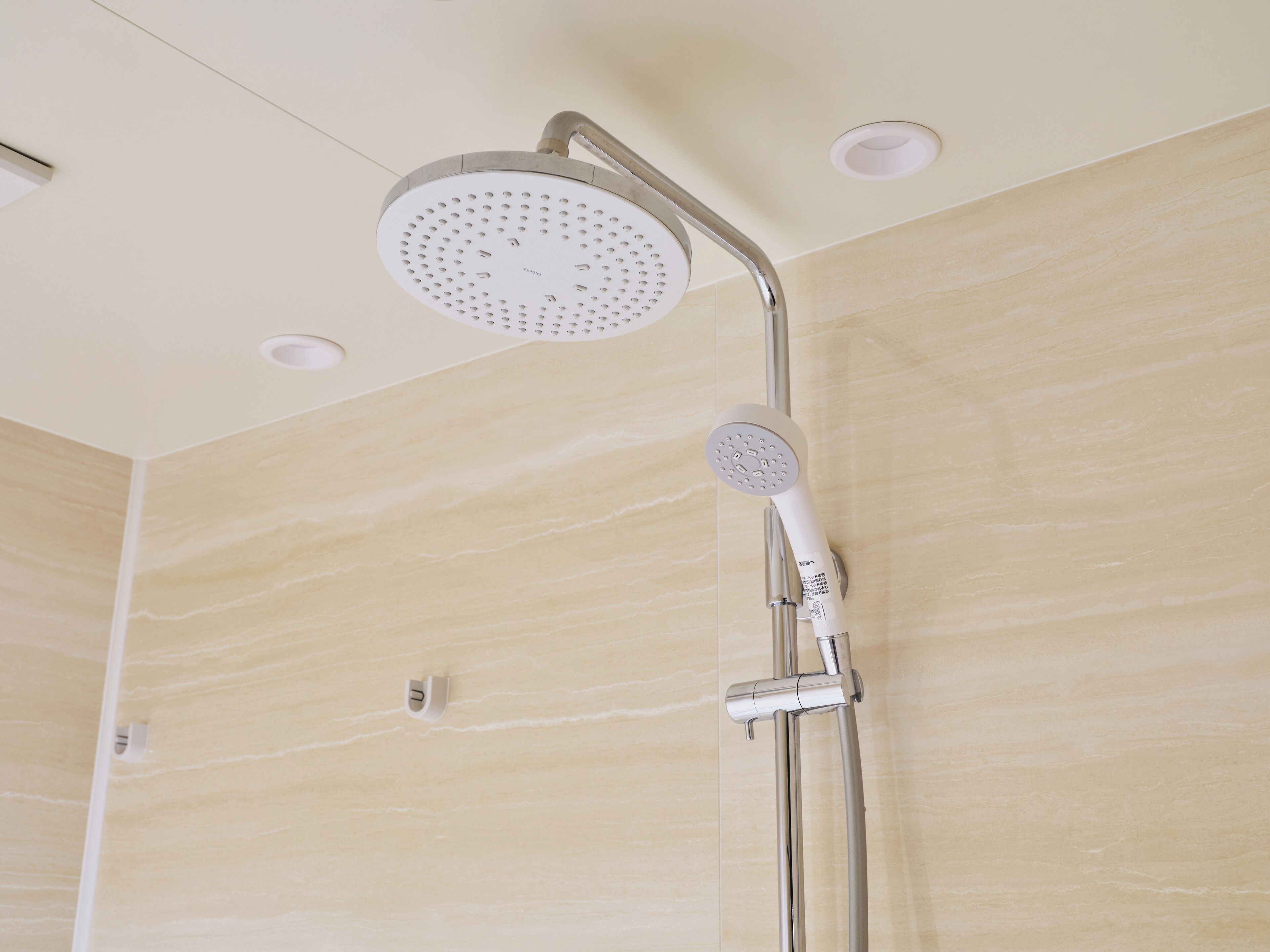 A modern showerhead with a handheld attachment, mounted on a wall with a marble-like finish.