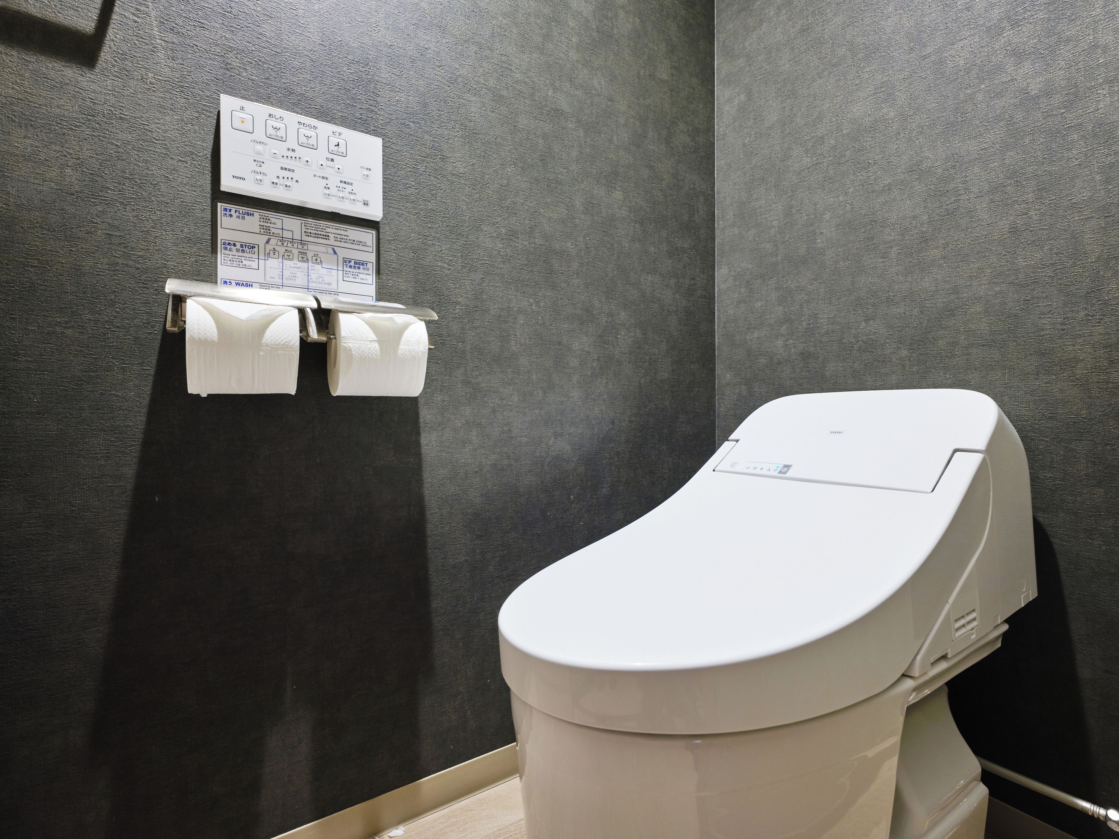 Un baño moderno con inodoro, dispensador de toallas de papel y un cartel con indicaciones.