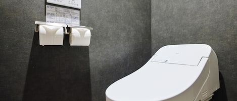 A modern bathroom with a toilet, a paper towel dispenser, and a sign with instructions.