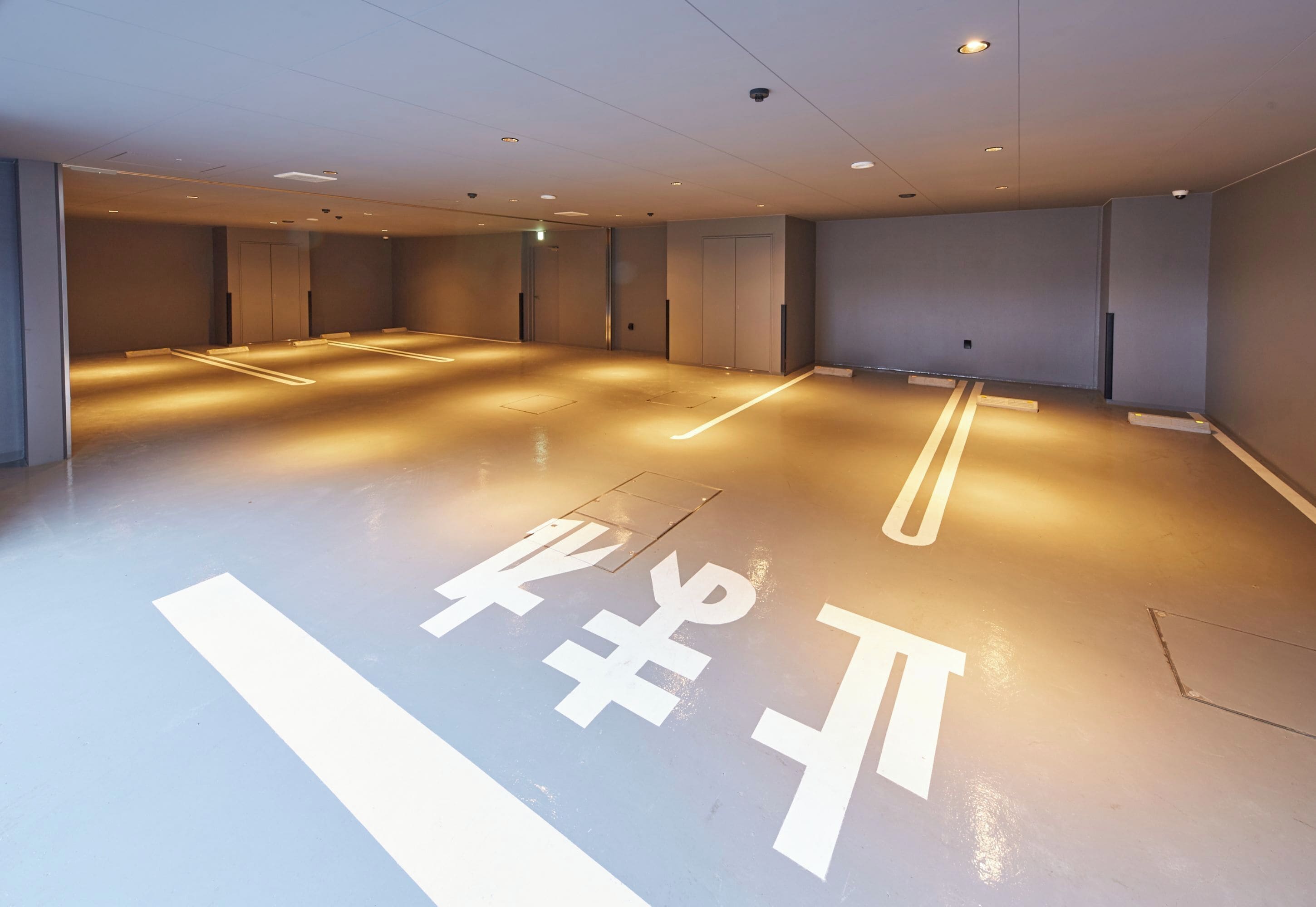 A spacious, modern hotel lobby with a clean, minimalist design, featuring a polished floor with directional markings and a neutral color palette.