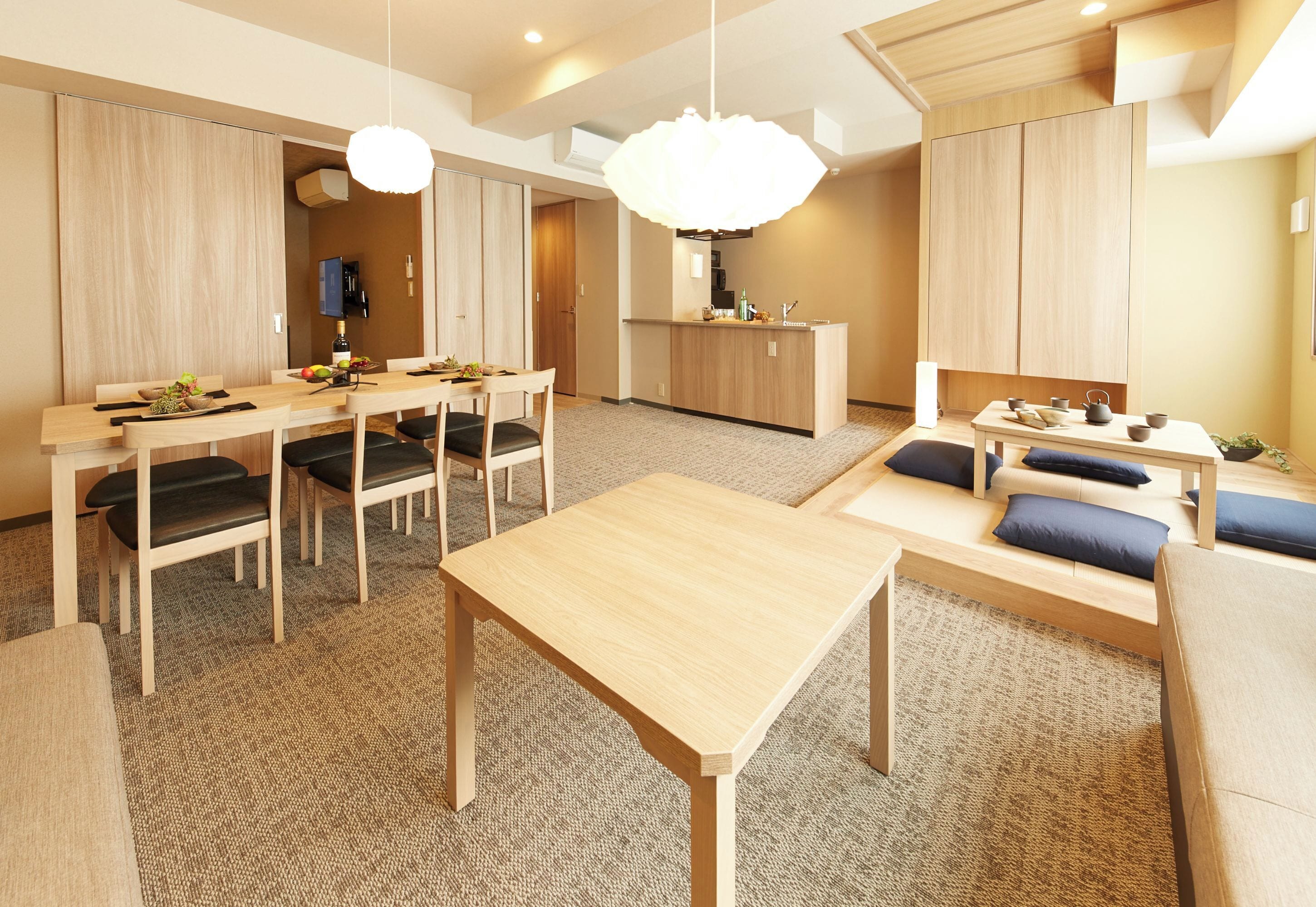 Moderni hotellihuone, jossa on ruokailutila, pieni keittiö sekä oleskelualue sohvineen ja tuoleineen.