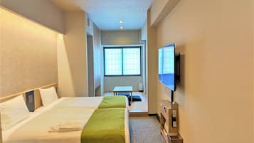 A hotel room with two beds, a TV, a desk, and a window.